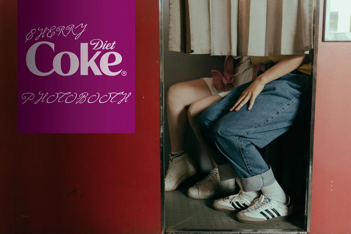 A red photobooth with a “Cherry Diet Coke Photobooth” sign; two people’s legs show beneath the curtain